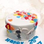 Colorful heart-shaped sugar cookies decorated on a white fondant cake for special celebrations.